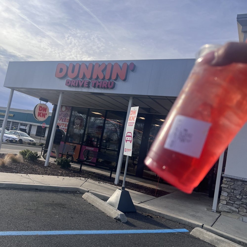 a person holding a drink in front of a dunkin donuts store a person holding a drink in front of a dunkin donuts store