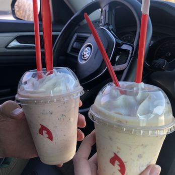 Apollo Burger - Strawberry/Reese's shake and a baklava shake! - Two milkshake cups with whipped cream and straws are held inside a vehicle, with a Volkswagen steering wheel visible. - Burgers Near Me - Lehi, Utah