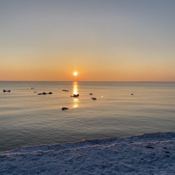 Foster Avenue Beach - 02/27/21 - Foster Avenue Beach just after sunrise, floating ice chunks in the lake - A sunset scene over a lake with floating ice chunks, a snow-covered shoreline, and a clear sky. - Beaches Near Me - Chicago, Illinois