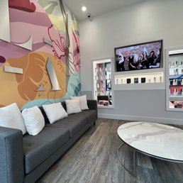 Lobby - A modern waiting room features a large floral mural on one wall, a gray sofa with white pillows, and a wall-mounted TV displaying a group photo.