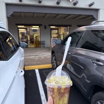 Juice Queen’s - Dubai chocolate strawberry - A hand holds a smoothie with a spoon in front of the Juice it up storefront, with parked cars and the shop entrance visible. - Juice Bars & Smoothies Near Me - Mesa, Arizona
