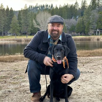 Nate Schoemer Dog Training - A man with his dog, posing in front of a lake. - Pet Training Near Me