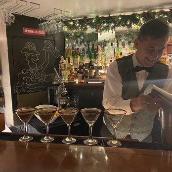 Anchor Bar - A bartender in formal attire, including a bow tie, is pouring a drink at a bar with numerous liquor bottles and festive decorations. - Bars Near Me - Baltimore, Maryland