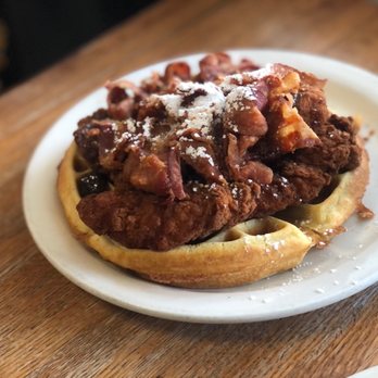 Fiddlestix Cafe - a plate of food on a table - A chicken and waffles dish with fried chicken, bacon, and powdered sugar served on a white plate at Fiddlestix Cafe in Cornwall, NY. - Breakfast & Brunch Near Me - Cornwall, New York