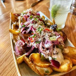 Carne Asada - A plate of carne asada fries with toppings like cheese, onions, and green onions, accompanied by a glass of water with lime slices.