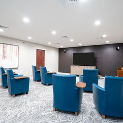 Vista Prairie at Copperleaf - A clean, spacious media or classroom setting. Teal blue leather armchairs with built-in wooden tablet arms are arranged in ro...