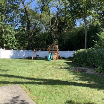 Express Tree Services - A backyard features a wooden playset with a slide and swings, enclosed by a white fence and bordered by trees and shrubs. - Tree Services Near Me - Freeport, New York