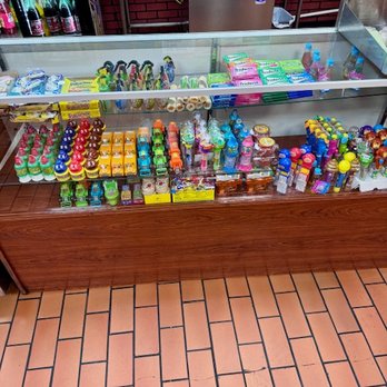 Las Brazas - A glass display case contains assorted candies, snacks, and small toys, with a store environment visible in the background. - Mexican Near Me - Cicero, Illinois