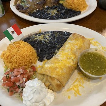 Freppe's Tex Mex - Our Cinco de Mayo dinner... Chimichanga and Steak Asado... Everything was delicious! Definitely recommend... - A Mexican dish featuring a burrito, yellow rice, black beans, salsa, sour cream, and green sauce, with a small Mexican flag on the plate. - Tex-Mex Near Me - Plainfield, New Jersey