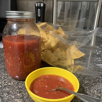 Ed & Judie's Egg Farm - Home made Salsa. Very good!!!!!! - A jar of homemade salsa, a yellow bowl of salsa with a spoon, and a bag of tortilla chips are placed on a kitchen countertop with a knife block and electrical outlet in the background. - Farmers Market Near Me - Aurora, Illinois