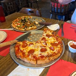 two pizzas on pans on a table