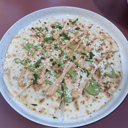 Chicken Quesadilla - A quesadilla cut into slices, served on a white plate, garnished with green herbs, drizzled with sauce, and sprinkled with cheese.