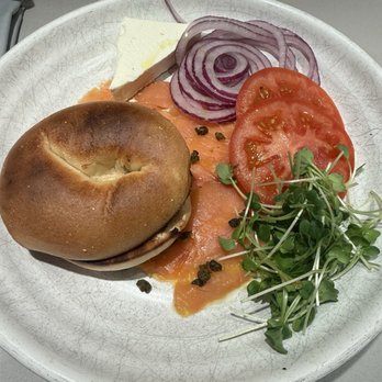 Kestra - A plate featuring smoked salmon, a bagel, sliced tomato, red onion, microgreens, and a piece of cheese, served on a white dish. - New American Near Me - Boston, Massachusetts
