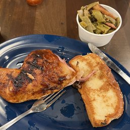 Texas Toast - A plate contains a grilled chicken leg with char marks, a grilled cheese sandwich with toasted bread, and a white cup filled with cooked green beans. Small containers of sauce are visible on the table in the background. The setting appears to be a casual dining environment.