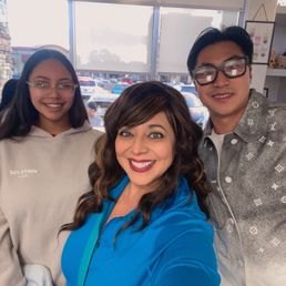 A woman and two young individuals take a selfie inside a store with large windows and parked cars outside.