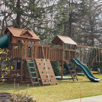 Creative Playthings - A huge wooden residential swing set with multiple gyms and many play accessories from Creative Playthings. Shown in a backyard on grass. - Playsets Near Me - Holliston, Massachusetts Creative Playthings - A huge wooden residential swing set with multiple gyms and many play accessories from Creative Playthings. Shown in a backyard on grass. - Playsets Near Me - Holliston, Massachusetts