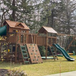Creative Playthings - A huge wooden residential swing set with multiple gyms and many play accessories from Creative Playthings. Shown in a backyard on grass.
