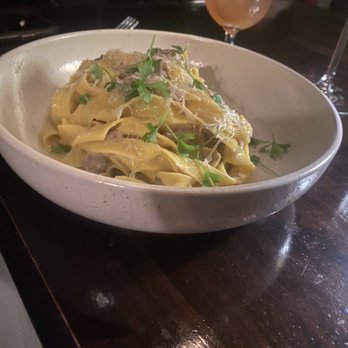 The Maker Restaurant - A dish of pasta with herbs served in a white bowl, accompanied by a cocktail in a glass with ice, on a dark wooden table. - Cocktail Bars Near Me - Hudson, New York