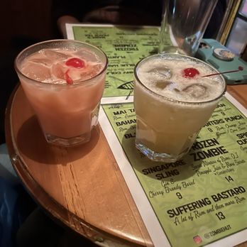 Zombie Hut - Two cocktails with ice and cherries are placed on a bar table at Zombie Hut, a tiki-themed bar in Brooklyn, NY, with a menu underneath. - Tiki Bars Near Me - Brooklyn, New York