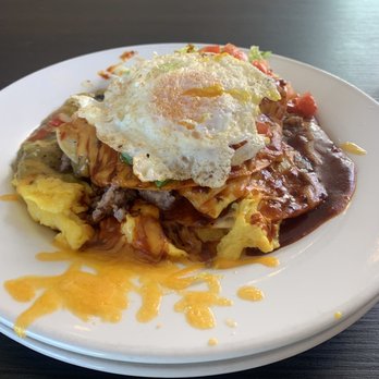 Joe's Dining - Breakfast enchilada - A breakfast dish featuring scrambled eggs, melted cheese, and a fried egg on top, served on a white plate. - Pizza Near Me - Santa Fe, New Mexico