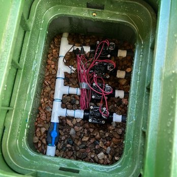 Alpha1 Sprinklers - An irrigation control setup with PVC pipes, solenoid valves, and wiring installed inside a green container, likely for landscape watering. - Irrigation Near Me - Albuquerque, New Mexico