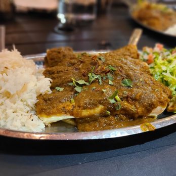 Nasha - Lamb Enchiladas with Verde Sauce - A metal plate holds rice, lamb curry with green herbs, a side salad, and guacamole, served in a restaurant setting. - Indian Near Me - Austin, Texas