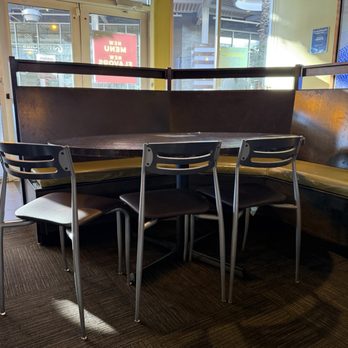 Noodles and Company - A booth with three chairs is positioned around a dark wooden table inside a restaurant, near glass doors and windows that let in natural light. - Noodles Near Me - Tempe, Arizona