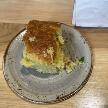 Zynda's - Jalapeño cornbread - A slice of jalapeño cornbread with a golden-brown crust on a ceramic plate, placed on a wooden table. - Cocktail Bars Near Me - Williamston, Michigan