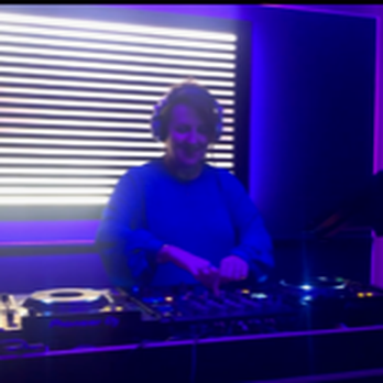 Pirate Studios - A DJ is performing in a dimly lit room with purple and blue lighting, standing behind DJ equipment with a striped light panel in the background. - Recording & Rehearsal Studios Near Me - Brooklyn, New York