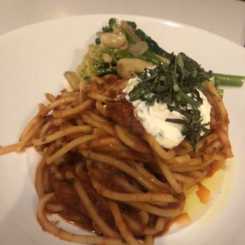 Holman's Table - Pasta - A white plate contains a serving of spaghetti noodles coated in a tomato-based sauce, topped with chopped herbs and a dollop of sour cream. The dish is accompanied by steamed broccoli, cauliflower, and other vegetables. The presentation emphasizes the pasta as the main focus, with the vegetables arranged around it. - Bars Near Me - Saint Paul, Minnesota