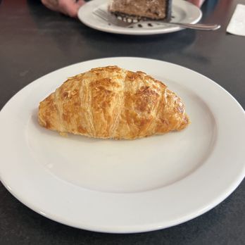 Joe's Dining - A flaky, golden croissant is placed on a white plate, with a slice of layered cake in the background on another plate. - Pizza Near Me - Santa Fe, New Mexico