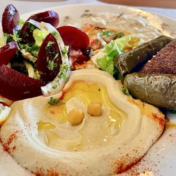 Damashkey Cuisine - A plate featuring hummus with olive oil and chickpeas, grape leaves, stuffed vegetables, a salad with onions and tomatoes, and a lemon wedge. - Mediterranean Near Me - Lindenhurst, Illinois
