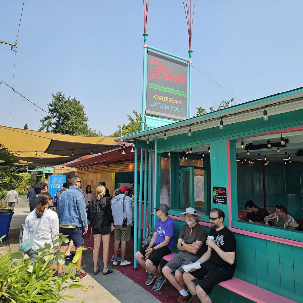 Un Bien - a group of people sitting outside of a restaurant - Caribbean Near Me - Seattle, Washington