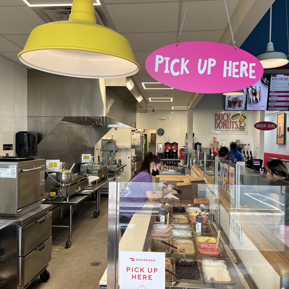 Duck Donuts - A customer stares in amazement as the worker, in her natural habitat, carefully brushes toppings onto a warm freshly baked baked donut - Donuts Near Me - Paramus, New Jersey