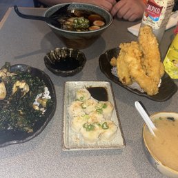 Japanese cuisine with tempura, sushi, and ramen served on black and ceramic dishes at a restaurant table.