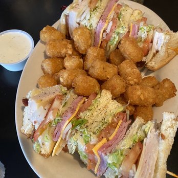 Pub 212 - Club House Sandwich* - A plate features club sandwiches with layers of meats, cheese, lettuce, and tomato, accompanied by fried chicken nuggets and a side of creamy dipping sauce. - American Near Me - Damascus, Oregon