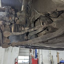 Not done at all, tie rod - View of a vehicle's suspension and steering system, including tie rods and control arms, in a garage setting.