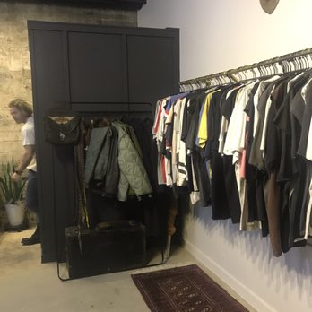 Hide & Hunter - A clothing rack displays assorted shirts and jackets in a retail setting, with a black storage cabinet and a decorative deer head on the wall. - Leather Goods Near Me - Birmingham, Alabama