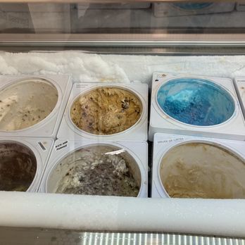 Bee Sweet - More flavors - A freezer display case contains several tubs of ice cream flavors, including chocolate, cookie dough, blue raspberry, and vanilla. The tubs are arranged in two rows, with the ice cream visible through the clear glass lid. The display case has a white foam border and is situated in a retail environment, likely an ice cream shop. - Ice Cream & Frozen Yogurt Near Me - St. George, Utah