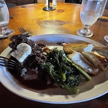Johnny Seesaw's - Steak frittes with filet mignon and yummy potatoes and broccolini. - A dinner plate with steak, broccolini, and potato slices is set on a wooden table, accompanied by water glasses and utensils. - American Near Me - Peru, Vermont