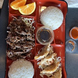a tray of food with rice, meat, and orange slices
