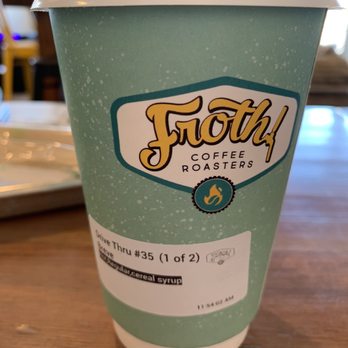 Froth Coffee Roasters - A paper coffee cup from Froth Coffee Roasters with a lid, placed on a wooden table, featuring the company's logo and a label with order details. - Coffee & Tea Near Me - Phoenix, Arizona