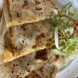 Quesadillas - Three quesadillas with golden-brown, slightly crispy tortillas and melted cheese are arranged on a white plate. The quesadillas contain green peppers and are served with a side of shredded lettuce and chopped tomato. The image captures a close-up view of the dish, highlighting the texture of the tortillas and the fresh salad garnish.