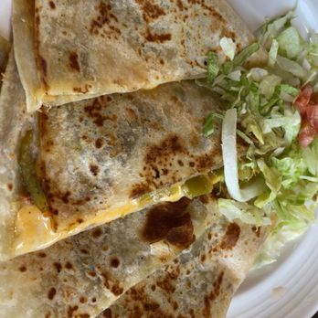 Someburros - Green chile quesadilla - Three quesadillas with golden-brown, slightly crispy tortillas and melted cheese are arranged on a white plate. The quesadillas contain green peppers and are served with a side of shredded lettuce and chopped tomato. The image captures a close-up view of the dish, highlighting the texture of the tortillas and the fresh salad garnish. - Mexican Near Me - Buckeye, Arizona