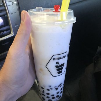 Boba Bee - Coconut boba tea smoothie with classic boba - A person holds a large bubble tea from Boba Bee, featuring black tapioca pearls at the bottom and a yellow straw, inside a vehicle. - Bubble Tea Near Me - Provo, Utah