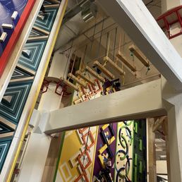Interior space featuring vibrant geometric wall art and suspended wooden swings, with structural beams and seating visible.