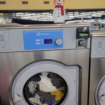 Laundry Palace - A snowman decoration with a red scarf and orange hat is positioned on top of an Electrolux washing machine in a laundromat. - Laundry Services Near Me - Riverhead, New York