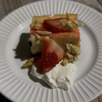 Tocoi Feed Mill - Keylime pie with strawberry and a chocolate almond crust - A slice of key lime pie with a graham cracker crust is presented on a white, ridged plate. The pie is garnished with fresh strawberries and sliced almonds on top. A dollop of whipped cream is placed beneath the pie, and the plate is set on a wooden surface. The background is blurred, focusing on the dessert. - Livestock Feed & Supply Near Me - Saint Augustine, Florida