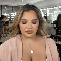 Makeup featuring warm smoky eyes, blended matte tones, full lashes, a rosy flush, and a glossy nude lip for a flawless, event-ready finish.