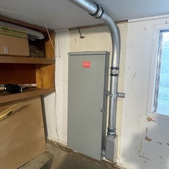 Hooked on Solar - Sub panel - A gray electrical panel with a red warning label is installed on a wall near a window, with metal conduit piping connected to it. - Solar Installation Near Me - Rocklin, California